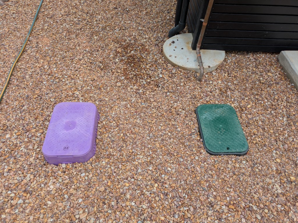 Purple and green valve boxes in the gravel beside the WWTP control room
